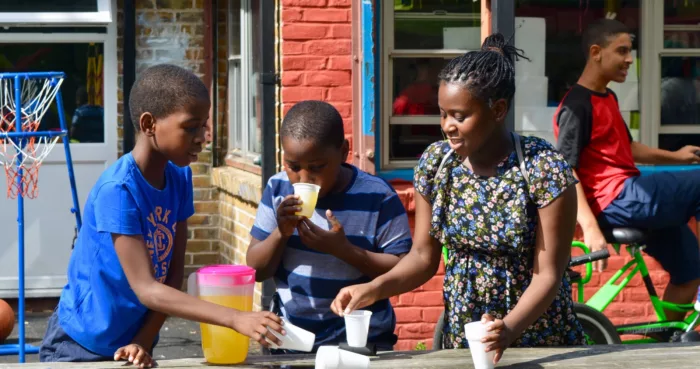 Three young people stand outside at a picnic table pouring drinks