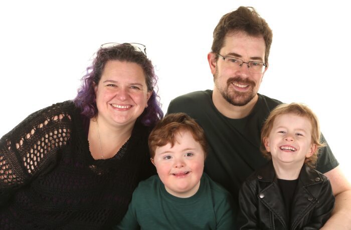 A family of four photographed together. There is a white background behind them