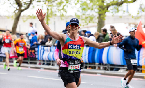 A runner in a Kids vest is running with his hands up in the air