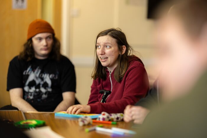 A young person is sitting around a table. They are speaking