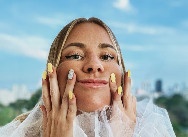 A young woman pushes the corners of her mouth up with her hands.