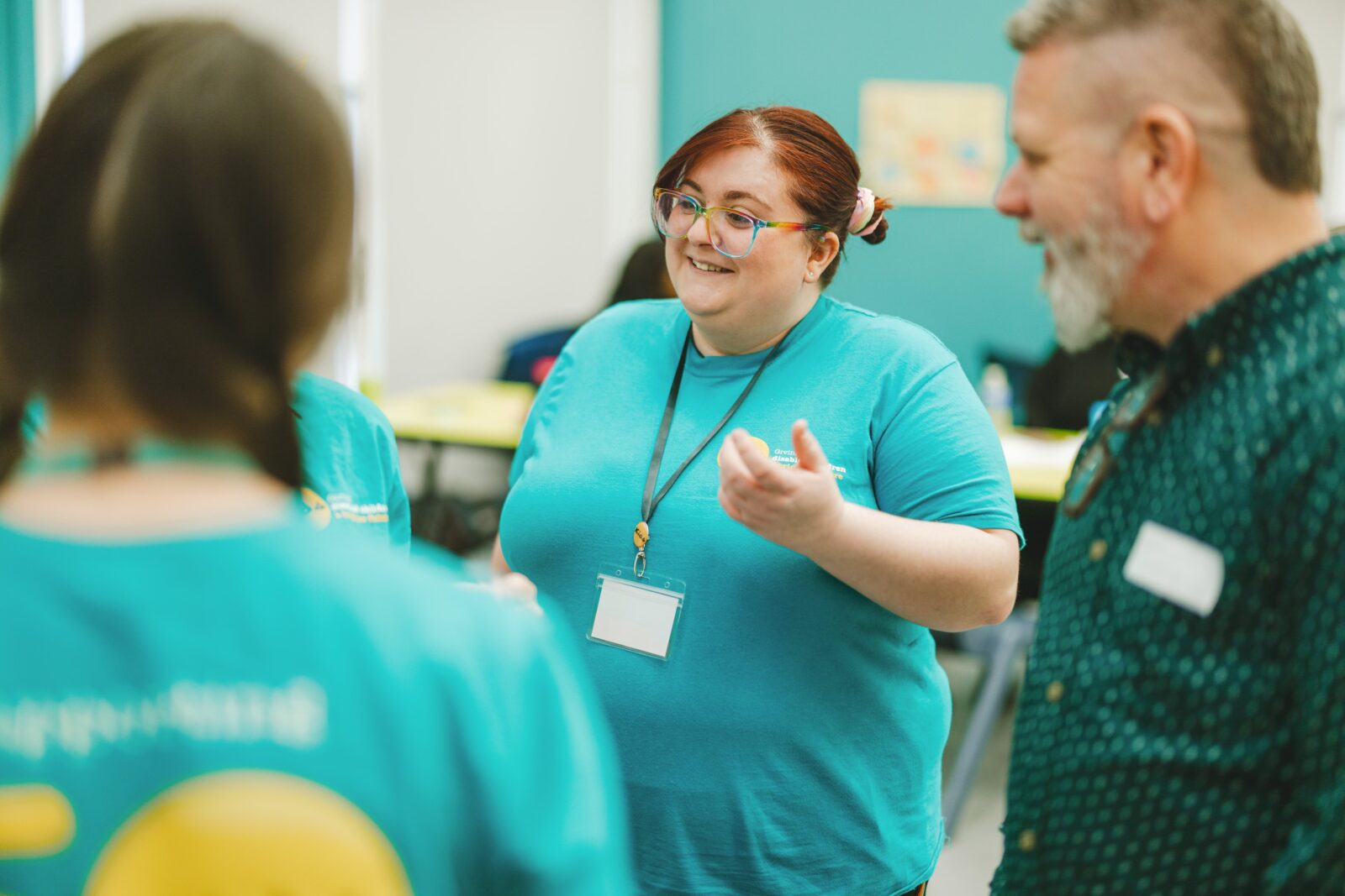 A Kids colleague is standing in a group of people. They seem to be talking at someone off camera. They are wearing a blue t-shirt